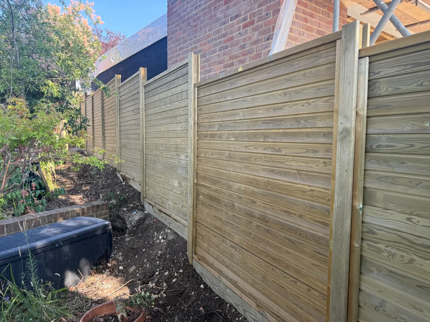 New horizontal slatted fence line beside a brick house in Farnham