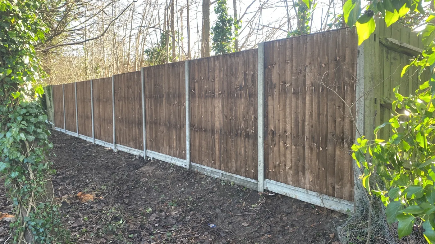 Long run of new dark stained fence panels installed along a woodland boundary
