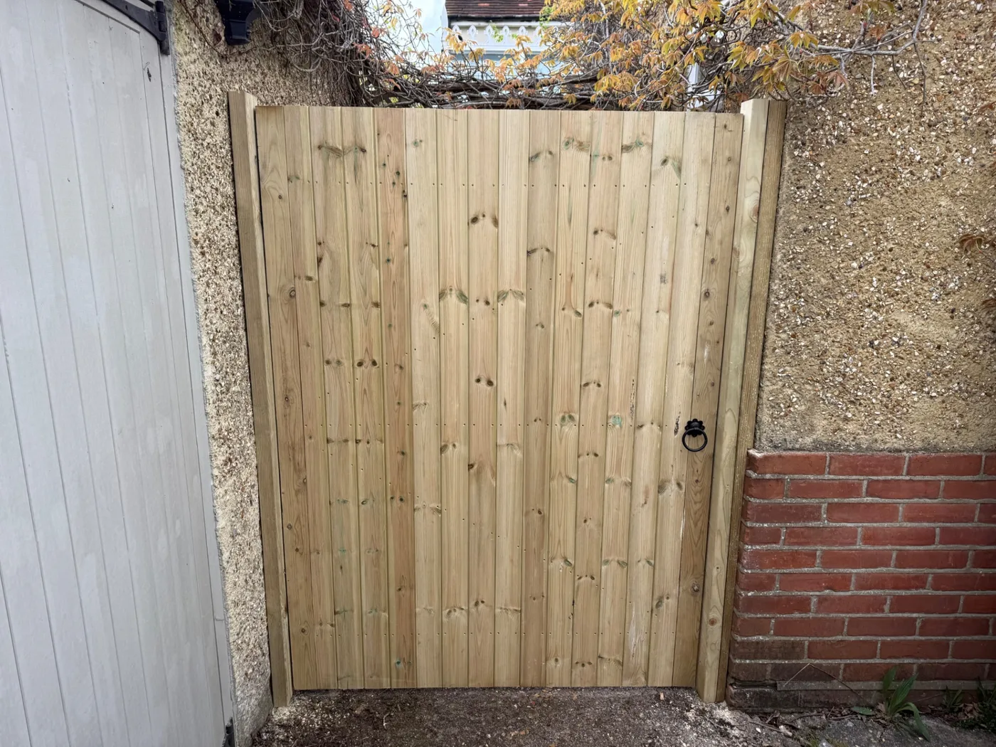 Tall timber side gate fitted between a garage and garden wall in Farnham