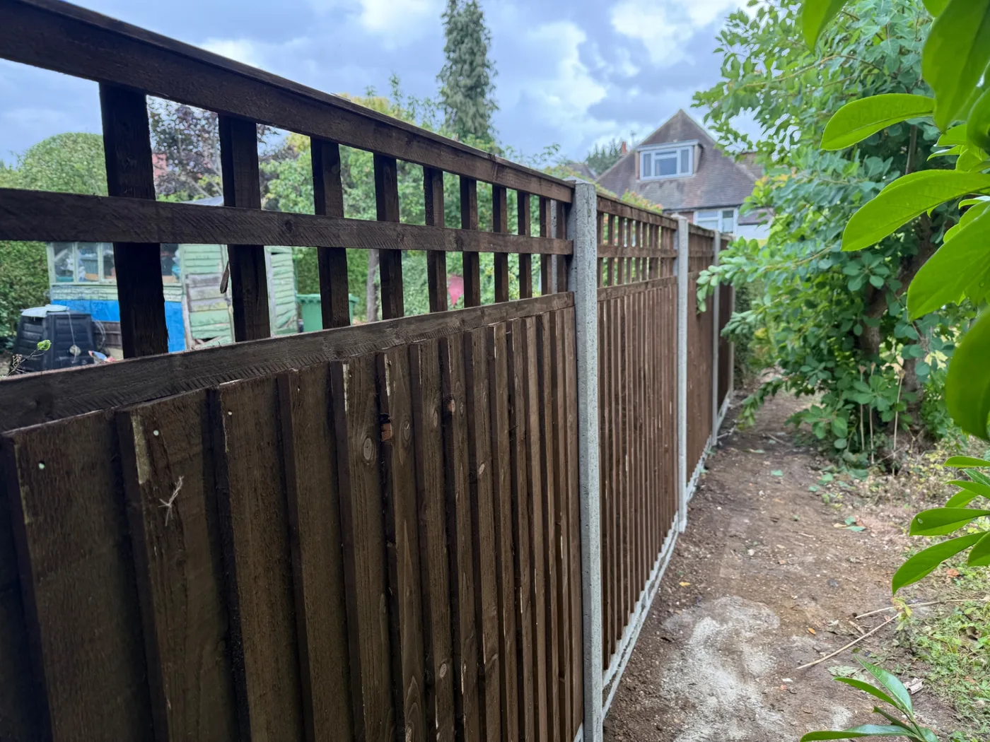 Dark stained feather edge fence panels with square trellis tops and concrete posts