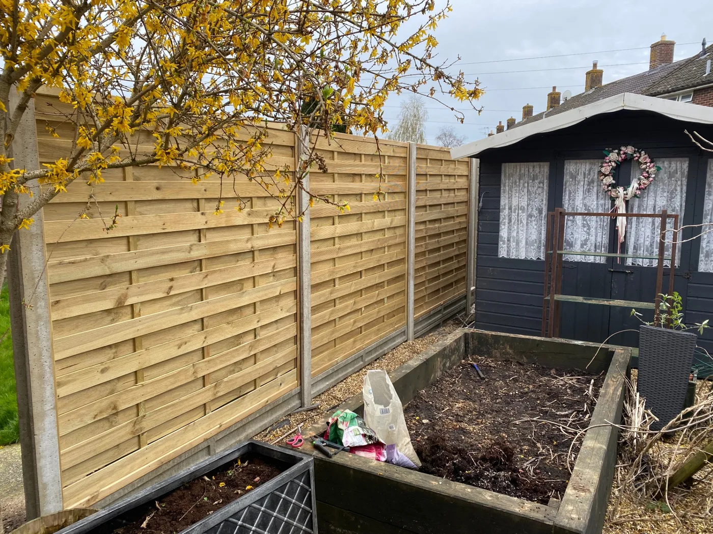 Woven horizontal fence panels with concrete posts beside raised beds in a Farnham garden